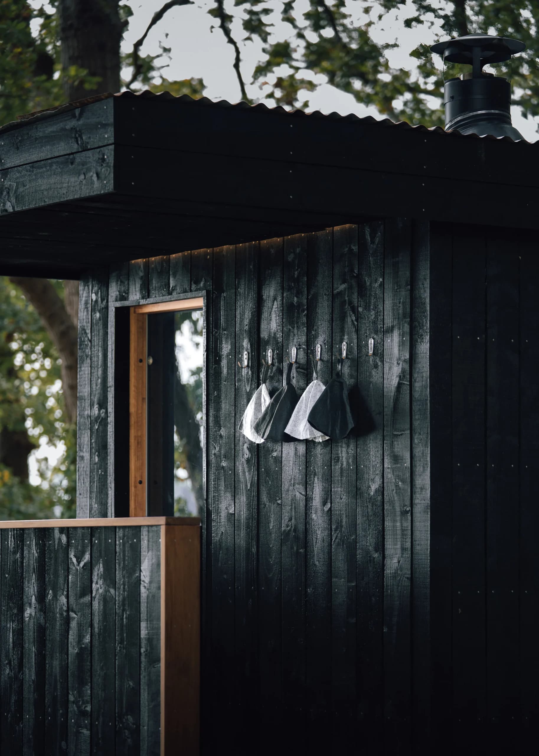 Black timber cladding on the Bosham Sauna, with felt sauna hats hung by the cedar-framed door.