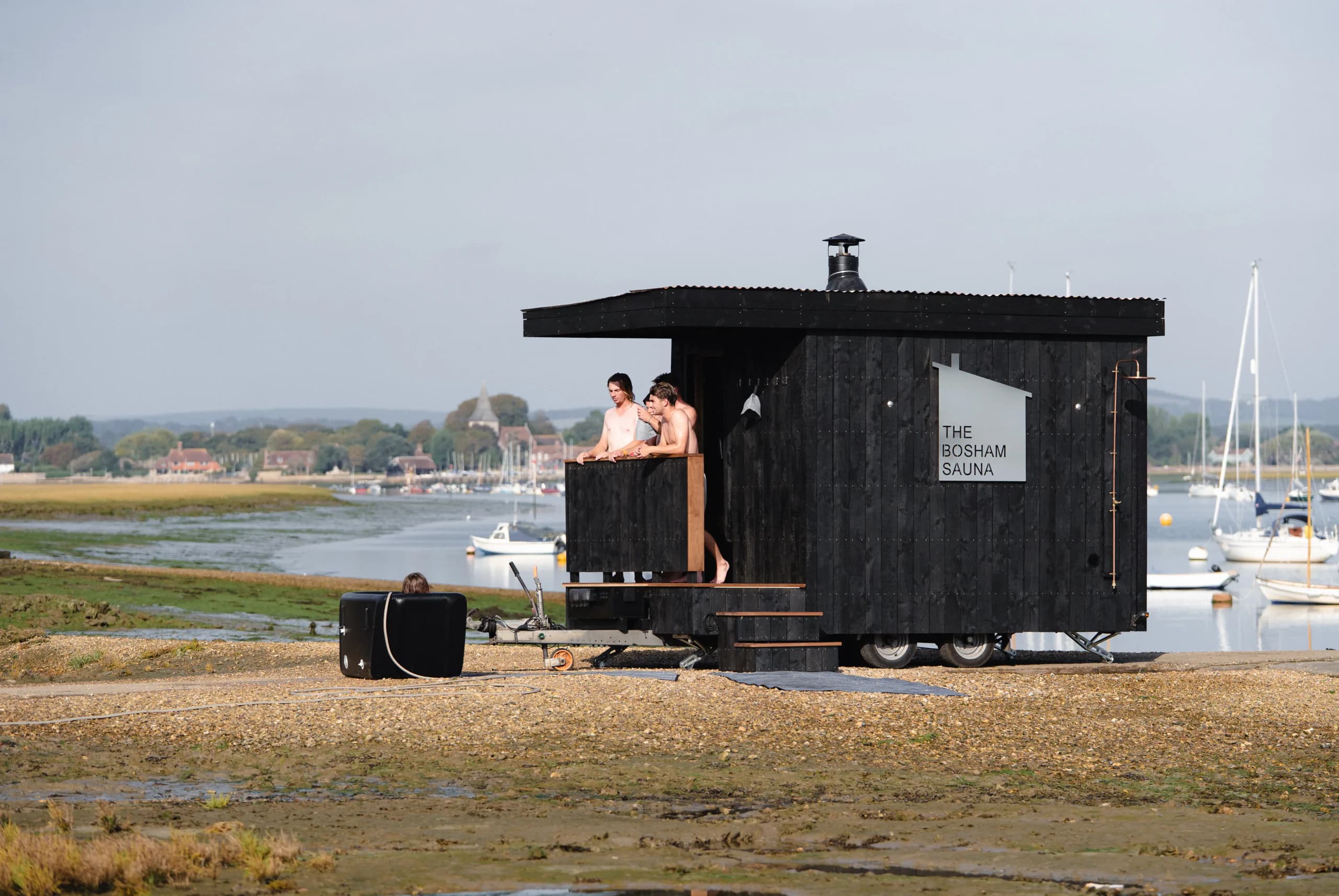 Two people on the Bosham Sauna porch at the water's edge, looking out over the harbour.